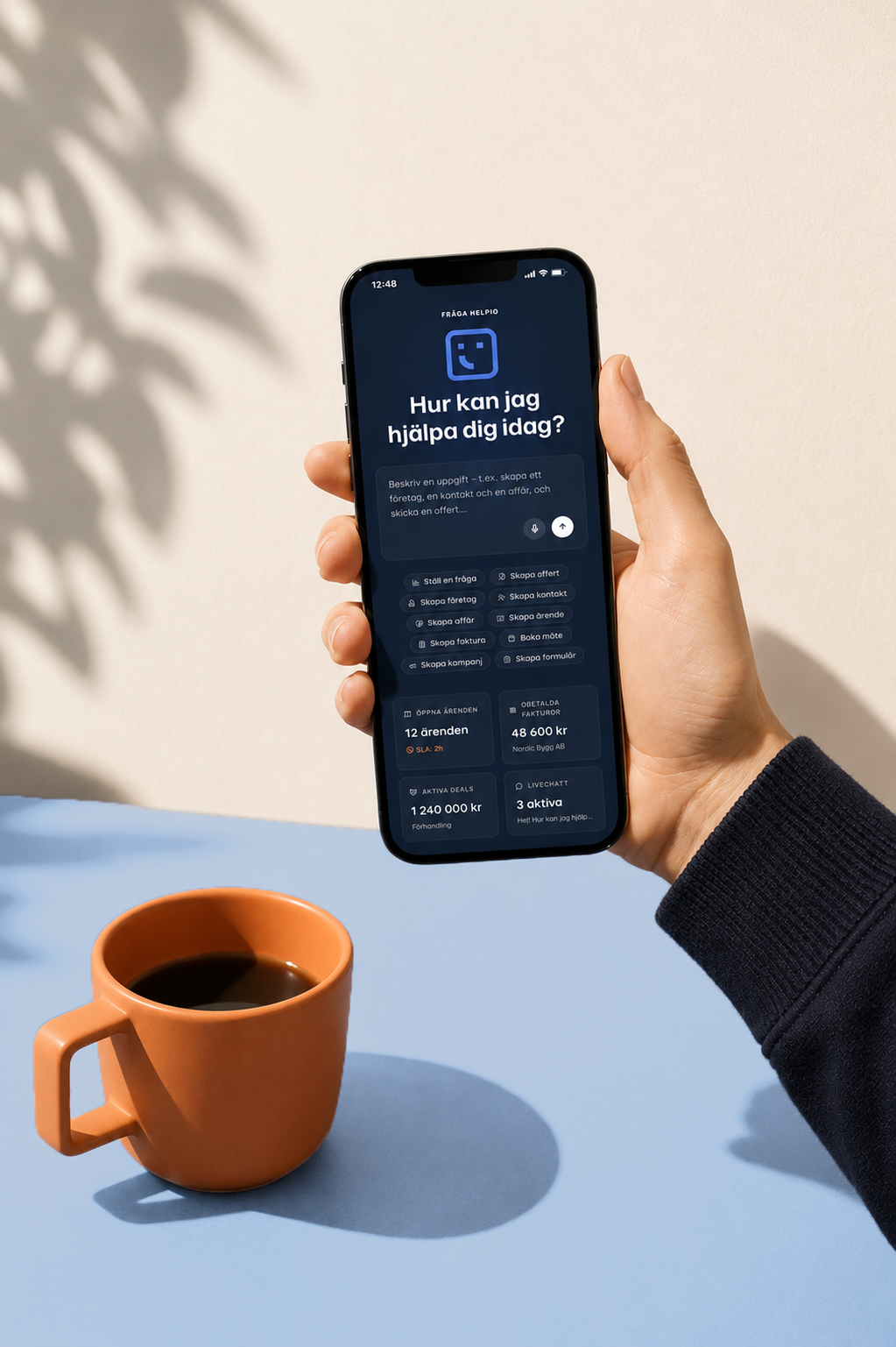 En hand håller en mobiltelefon med Helpio öppet bredvid en kaffekopp