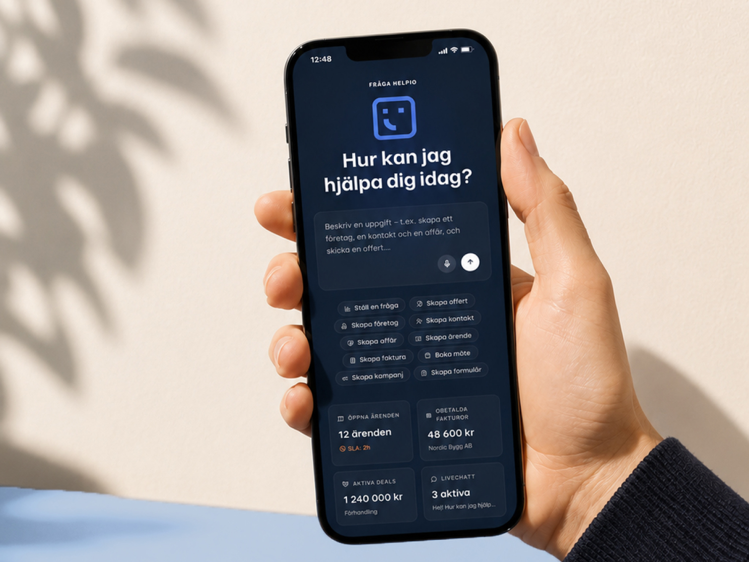 En hand håller en mobiltelefon där Helpio-chatten frågar ”Hur kan jag hjälpa dig idag?”